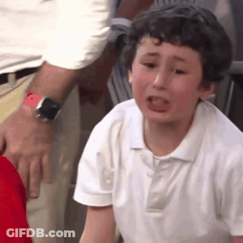A Young Boy In A White Shirt Is Crying While A Man Holds His Arm . GIF