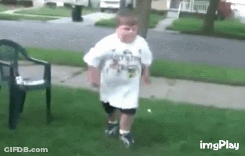 A Young Boy In A White Shirt Is Walking On A Sidewalk . GIF