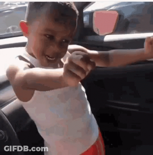 A Young Boy In A White Tank Top Is Standing In A Car With His Arms Outstretched GIF