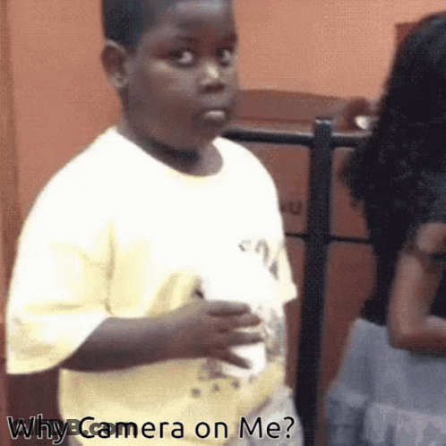 A Young Boy In A Yellow Shirt Is Holding A White Cup And Asking Why Camera On Me GIF