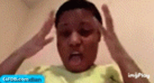 A Young Boy In A Yellow Shirt Is Making A Funny Face With His Hands On His Forehead . GIF