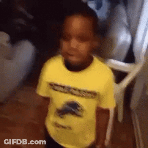 A Young Boy In A Yellow Shirt Is Standing In A Hallway . GIF
