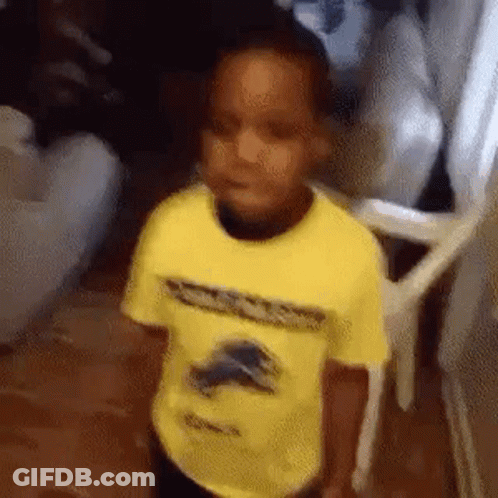 A Young Boy In A Yellow Shirt Is Standing In A Room . GIF
