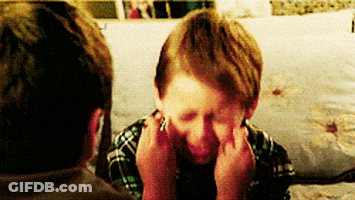A Young Boy Is Covering His Face With His Hands While Sitting On A Bed . GIF