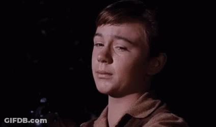 A Young Boy Is Crying In A Dark Room While Holding A Bottle . GIF
