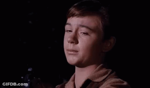 A Young Boy Is Crying In A Dark Room While Holding A Gun In His Hand . GIF