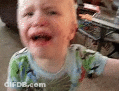 A Young Boy Is Crying On The Floor While Wearing A Dinosaur Shirt . GIF