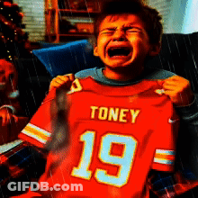 A Young Boy Is Crying While Holding Up A Toney 19 Jersey GIF