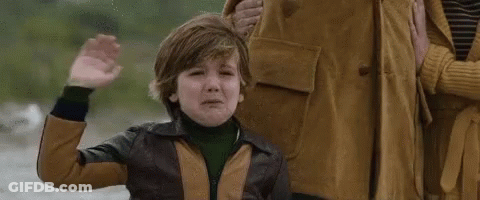 A Young Boy Is Crying While Standing Next To A Woman And Waving His Hand . GIF