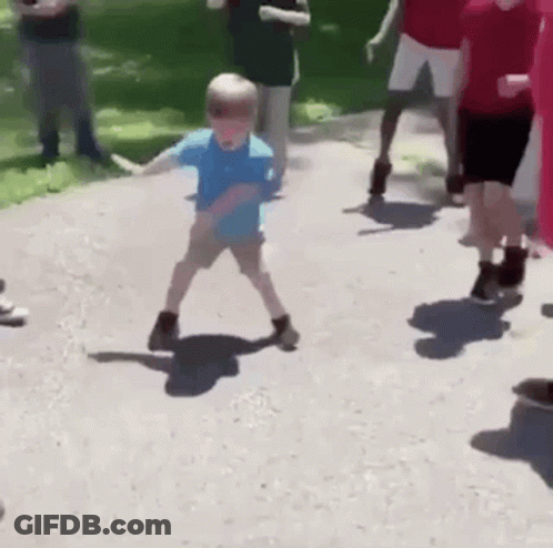 A Young Boy Is Dancing On A Sidewalk While A Group Of People Watch . GIF