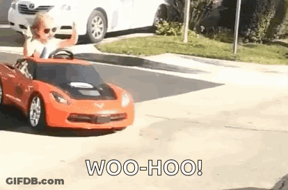 A Young Boy Is Driving A Toy Car Down A Street . GIF
