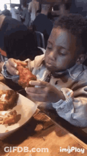 A Young Boy Is Eating A Chicken Wing At A Restaurant . GIF