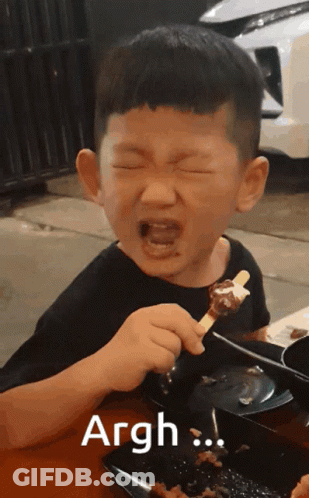 A Young Boy Is Eating A Skewer Of Food And The Word Argh Is On The Bottom GIF