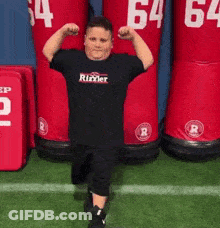 A Young Boy Is Flexing His Muscles In Front Of A Row Of Red Mannequins With The Number 64 On Them GIF