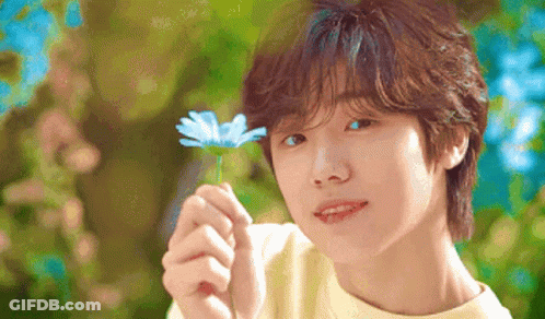 A Young Boy Is Holding A Blue Flower In His Hand And Smiling . GIF
