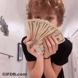 A Young Boy Is Holding A Fan Of Money In His Hands . GIF