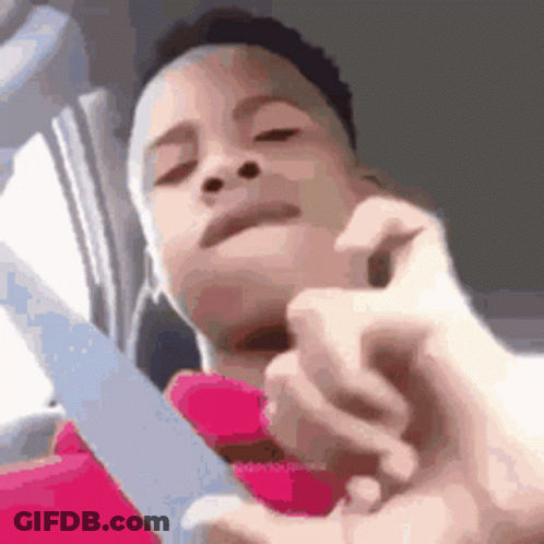 A Young Boy Is Holding A Knife In His Hand And Looking At The Camera . GIF