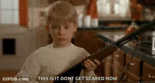 A Young Boy Is Holding A Shotgun In A Kitchen And Saying `` This Is It Do N't Get Scared Now '' . GIF