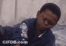 A Young Boy Is Laying On A Bed With His Eyes Closed And His Mouth Open . GIF