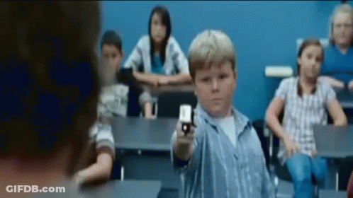 A Young Boy Is Pointing A Gun In A Classroom With Other Children GIF