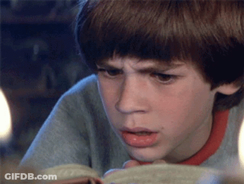 A Young Boy Is Reading A Book And Making A Funny Face GIF