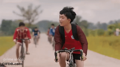 A Young Boy Is Riding A Bike Down A Dirt Road With Other People . GIF
