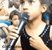 A Young Boy Is Singing Into A Microphone In A Crowd . GIF