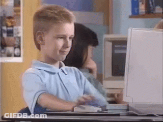 A Young Boy Is Sitting At A Desk Looking At A Computer Screen . GIF