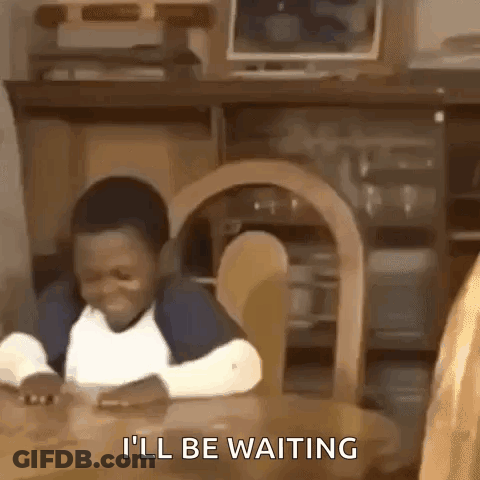 A Young Boy Is Sitting At A Table And Smiling While Waiting For Something . GIF