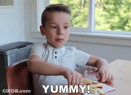 A Young Boy Is Sitting At A Table Cutting An Apple And Says Yummy ! GIF