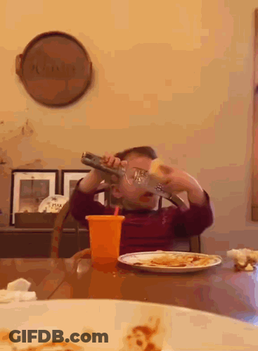 A Young Boy Is Sitting At A Table Drinking From A Bottle With A Straw GIF