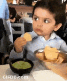 A Young Boy Is Sitting At A Table Eating Chips And Guacamole . GIF