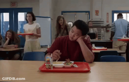 A Young Boy Is Sitting At A Table In A School Cafeteria Eating A Meal . GIF
