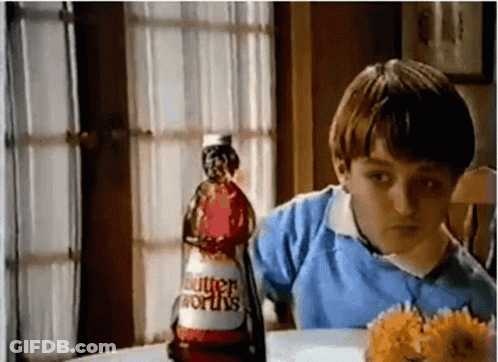 A Young Boy Is Sitting At A Table With A Bottle Of Butterworth 'S Ketchup . GIF