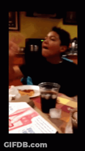 A Young Boy Is Sitting At A Table With A Cup Of Soda GIF