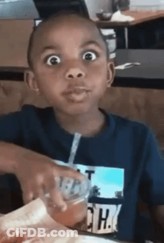 A Young Boy Is Sitting At A Table With A Straw In His Mouth . GIF