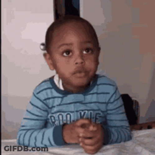 A Young Boy Is Sitting At A Table With His Hands Folded In Front Of Him . GIF