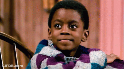 A Young Boy Is Sitting In A Chair Wearing A Purple And Blue Plaid Sweater GIF