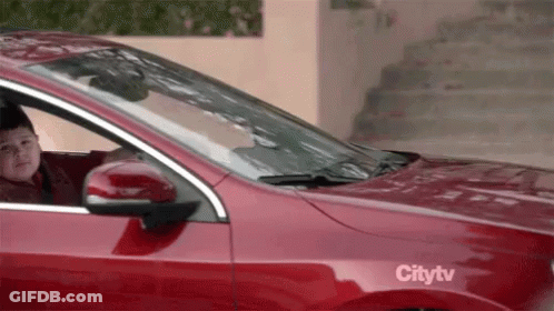 A Young Boy Is Sitting In A Red Car With A Citytv Sticker On The Side . GIF