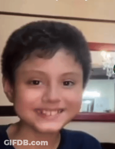 A Young Boy Is Smiling For The Camera In Front Of A Mirror In A Living Room . GIF