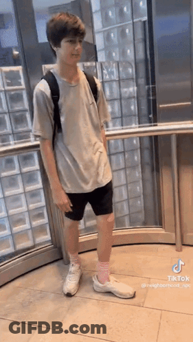 A Young Boy Is Standing In An Elevator Wearing Shorts And A Backpack . GIF