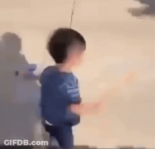A Young Boy Is Standing In Front Of A Wall And Holding A Remote Control . GIF