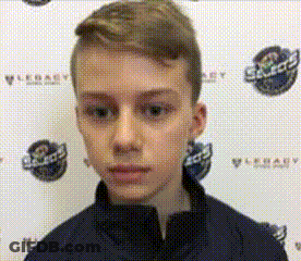 A Young Boy Is Standing In Front Of A Wall With Logos On It And Looking At The Camera . GIF