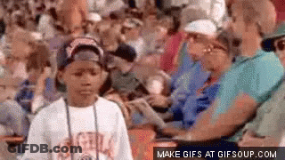 A Young Boy Is Standing In The Middle Of A Crowd Of People . GIF