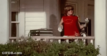 A Young Boy Is Standing On A Porch Wearing Sunglasses And A Red Tank Top . GIF