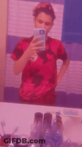 A Young Boy Is Taking A Selfie In Front Of A Mirror . GIF