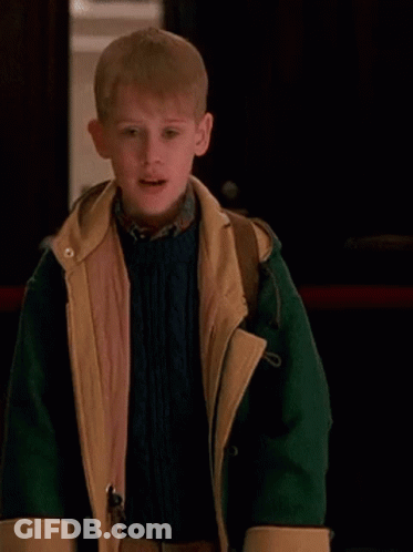 A Young Boy Is Wearing A Green And Yellow Jacket And A Blue Sweater . GIF