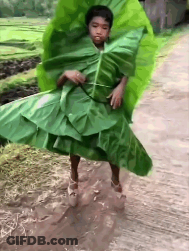 A Young Boy Is Wearing A Green Leaf Dress And High Heels GIF