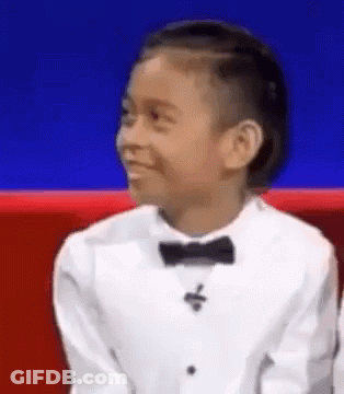A Young Boy Is Wearing A Tuxedo And Bow Tie And Smiling . GIF