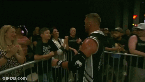 A Young Boy Kisses A Man On The Cheek In Front Of A Crowd GIF